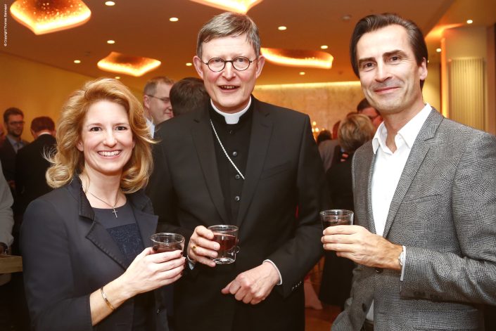 Nicole Grünewald und zwei Männer stoßen mit Gläsern bei einem Unternehmeressen an.