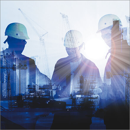 Drei Männer mit Bauhelmen stehen im Vordergrund, Hochhäuser sind im Hintergrund zu sehen.